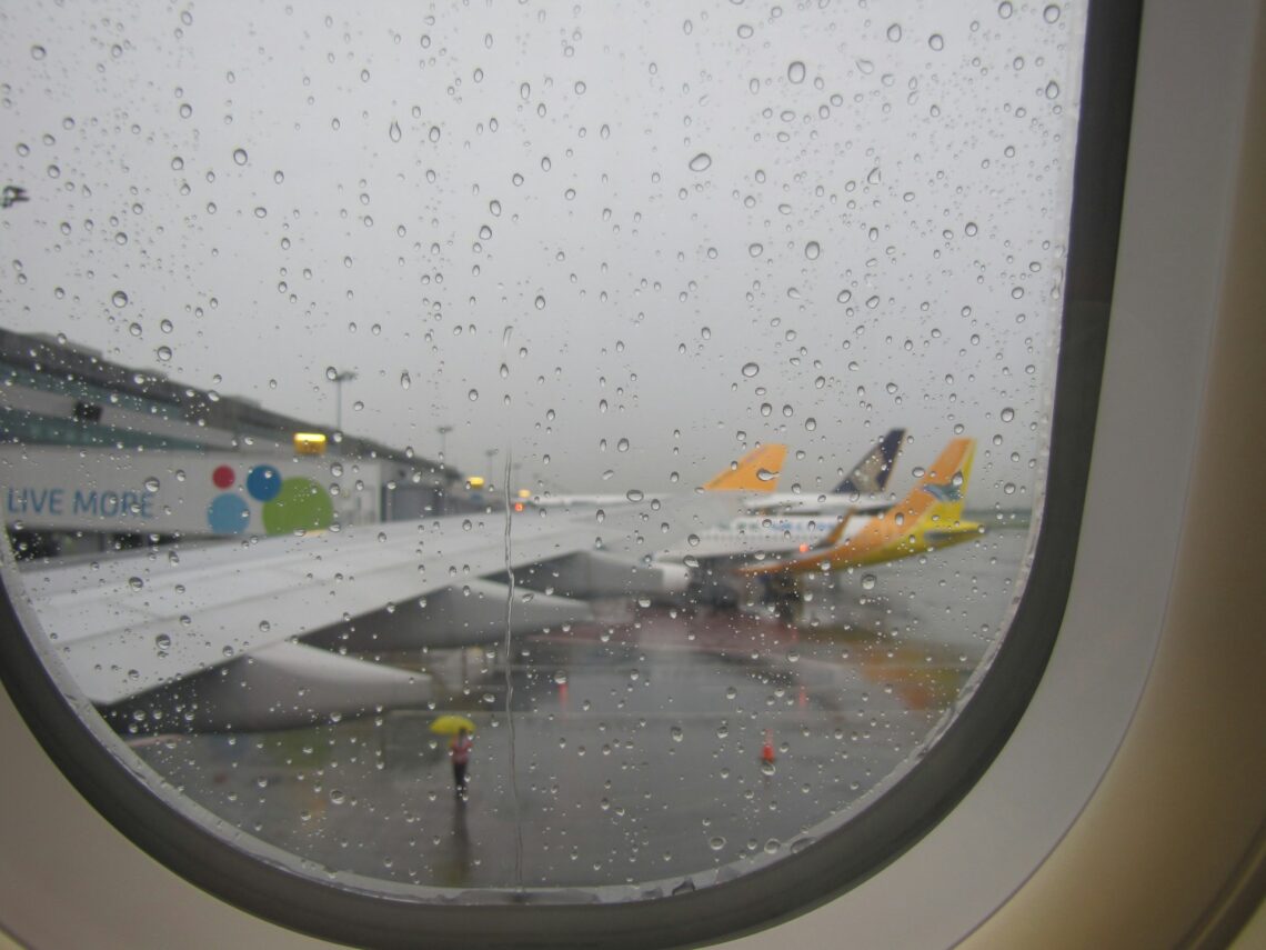 looking out a plane window at the airport with aircraft lined up at a gate in the rain