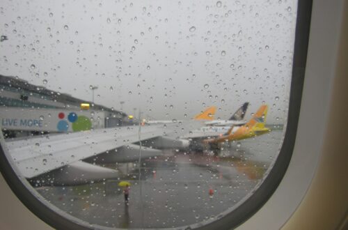 looking out a plane window at the airport with aircraft lined up at a gate in the rain
