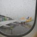 looking out a plane window at the airport with aircraft lined up at a gate in the rain