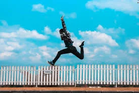 Person jumping high with blue skys beside a white picket fence