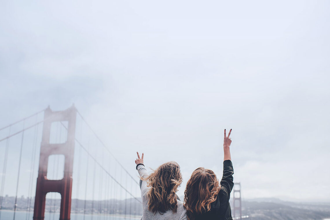 Two girls showing the peace sign with ther hand looking at the san Francisco golden gate bridge