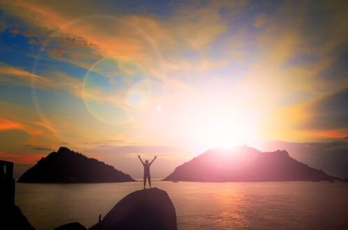 Person standing on a mountain with a sunrise with arms out with ocean and mountains