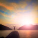 Person standing on a mountain with a sunrise with arms out with ocean and mountains