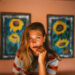 Girl with sunflower paintings behind on orange walls with a neutral face