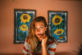 Girl with sunflower paintings behind on orange walls with a neutral face
