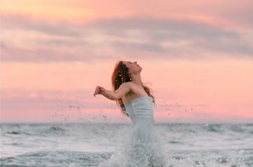 Woman Splashing through waves with beautiful sunrise arms out like letting go or freedom